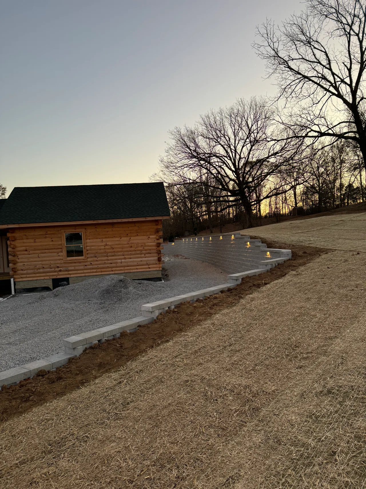 Block retaining wall curving beside a log home in the evening