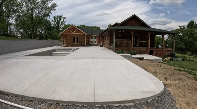 Broad concrete driveway curving in front of a log home with a retaining wall beside it